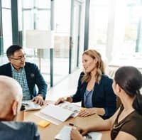 Eine Gruppe von Professionals sitzt in einem modernen, sonnendurchfluteten Büro an einem Konferenztisch und diskutiert engagiert über ein gemeinsames Projekt.